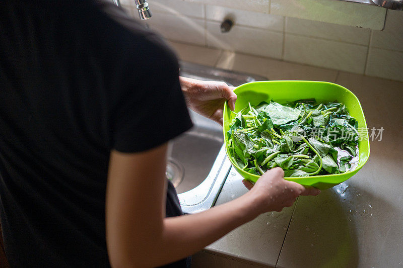年轻女子在厨房水槽里冲洗蔬菜