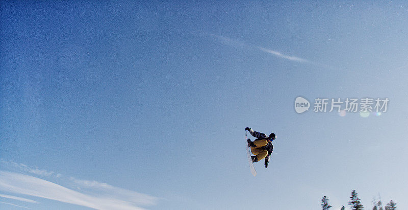 一个滑雪板在完整的冬季装备尝试“前侧360尾巴抓取”在跳跃在埃尔多拉滑雪度假村附近的博尔德，科罗拉多州在光明，阳光，冬天的一天