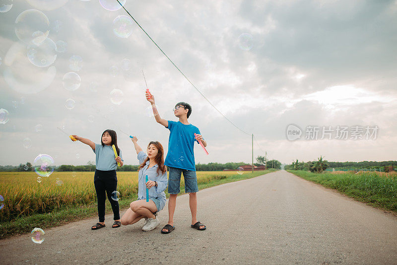 亚洲华人家庭花闲暇时间一起玩泡泡棒在乡村街道