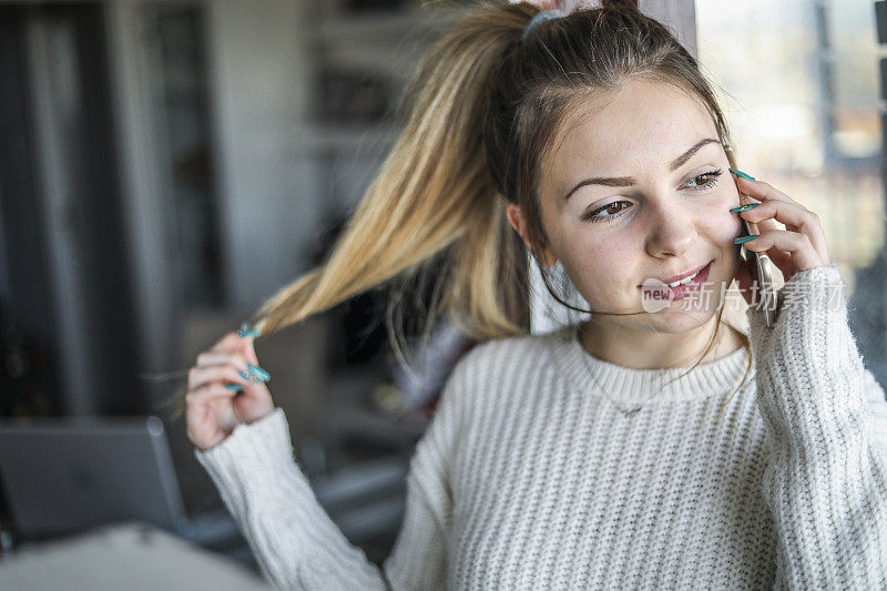 年轻女子在家里放松。一个十几岁的女孩正在用手机，站在阳台的门口享受美好的一天