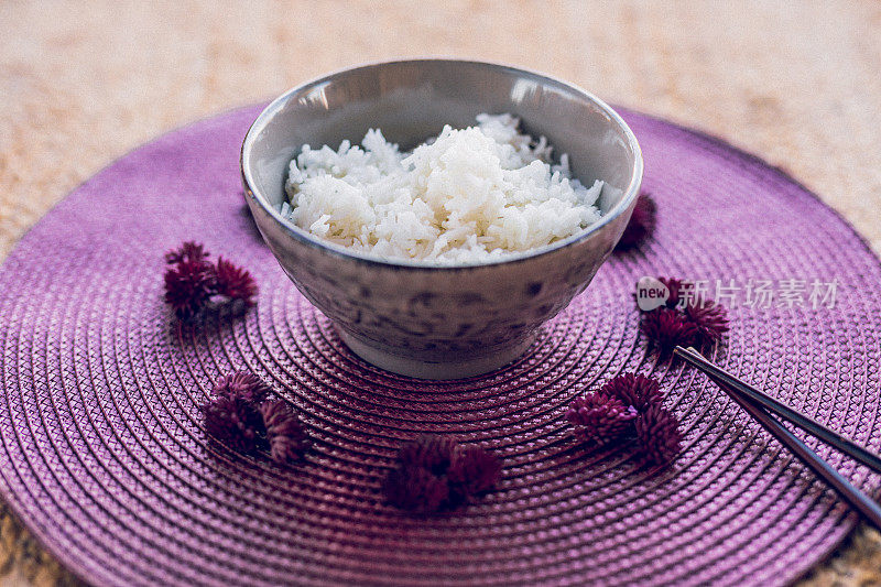 一碗亚洲米饭，上面有中国棍子，放在紫色的餐垫上