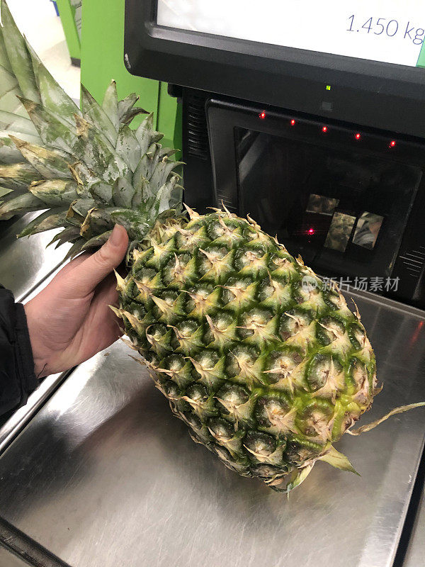 在超市自助结账处，一个不知名的人拿着菠萝进行扫描(自助结账)