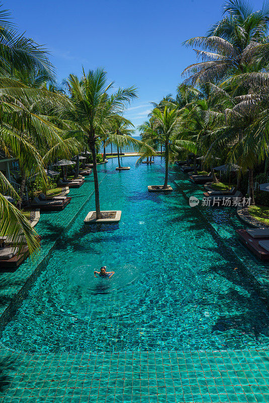 在海边游泳池度假村和酒店，游泳池的风景环绕椰子树和小屋。泳池边度假平房的游客在Hushin泰国
