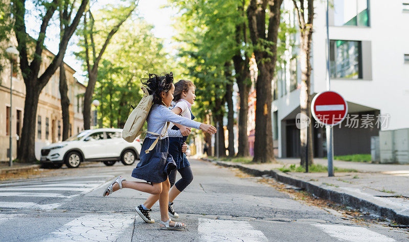 侧面的小女学生穿过街道在城外，跑步。