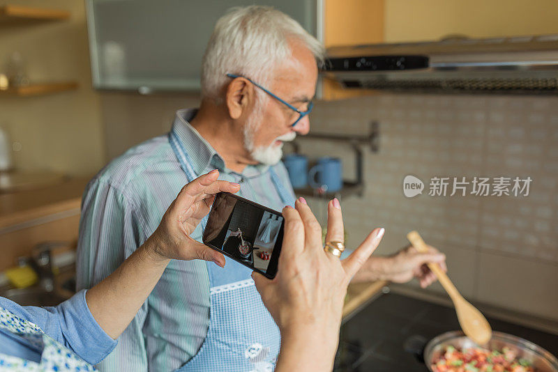 一位老年妇女正在拍摄她的丈夫准备食物。