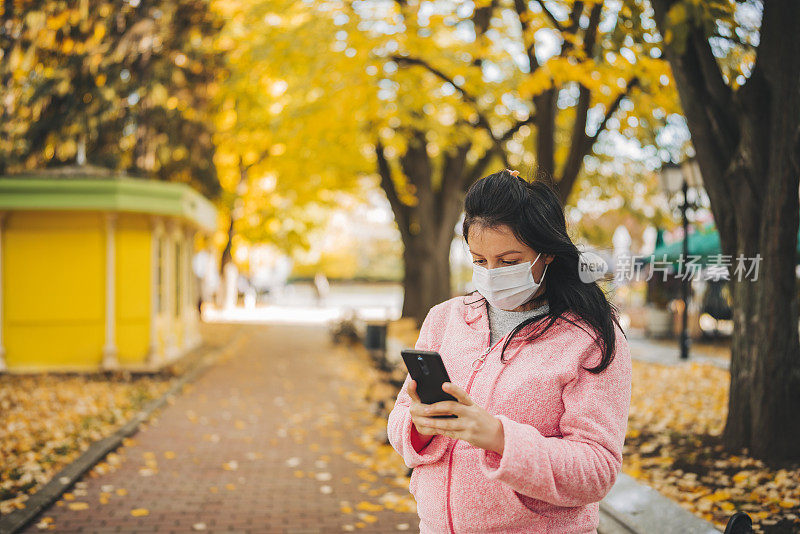 戴着口罩在城市公园里打电话的女人