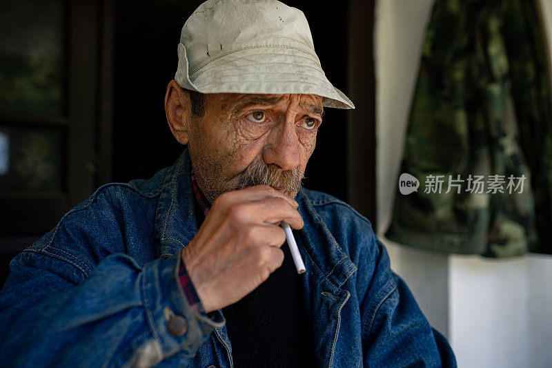 一个抑郁的老人在他老房子的门廊上抽烟
