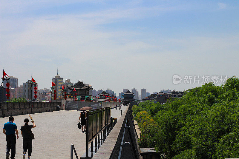 西安市宽阔的古城墙上挂着中国传统的红色灯笼，人们走在上面，映衬着蓝天。西安。中国