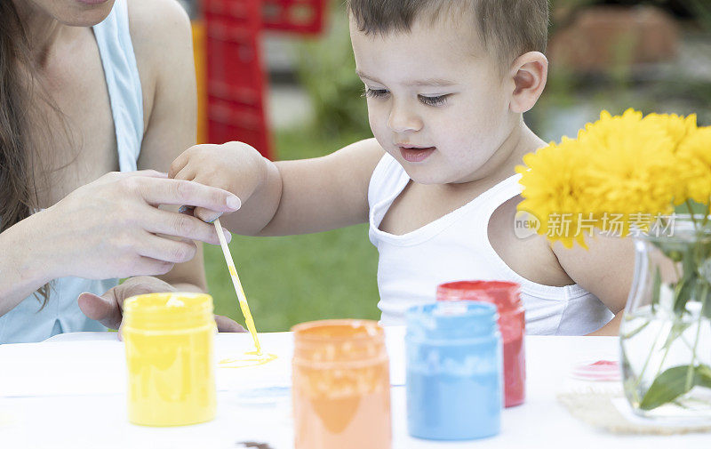 一个可爱的小男孩用画笔画画。绘画的乐趣。一个小男孩在家里的花园里画画。