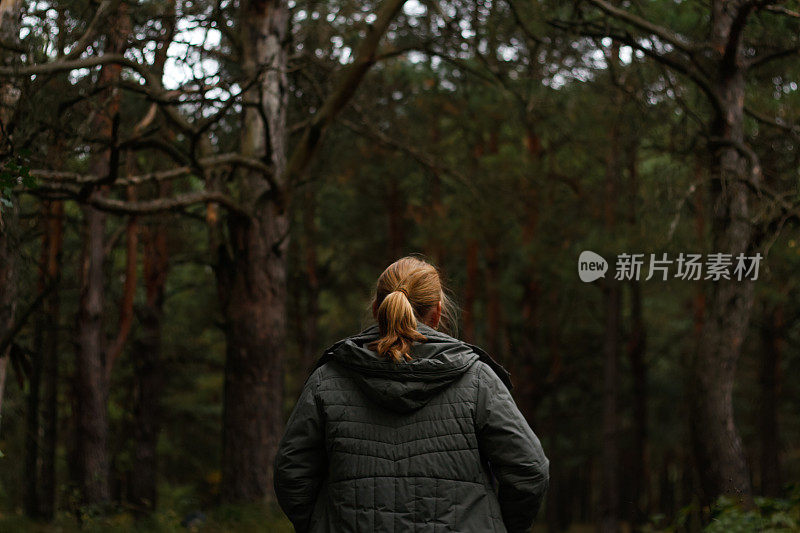 一个年轻的金发女人在森林里徒步旅行。徒步旅行的女人行走在黑暗神秘的森林，电影。人发现自然。黑暗的森林。的焦点