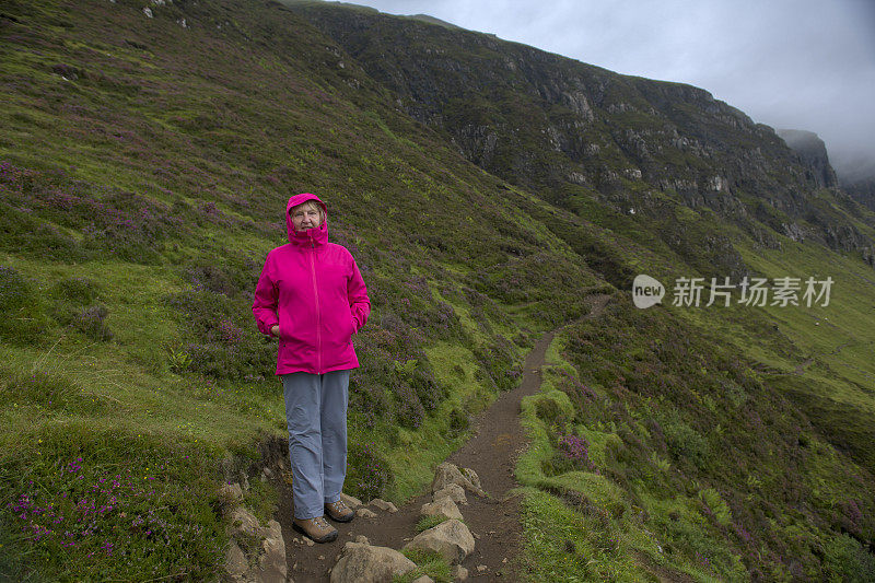 一位资深女性徒步旅行者在苏格兰Skye岛的Cuith-raing山脉徒步时，对着镜头微笑。