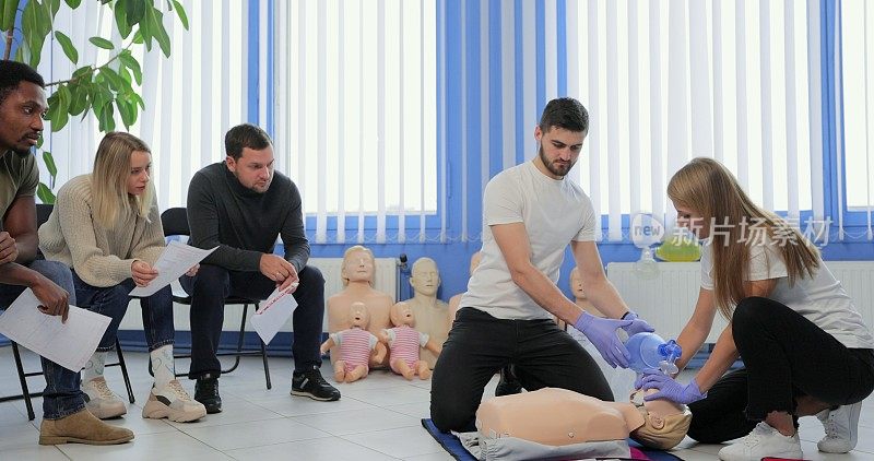 在室内急救课上，一群人在教练的指导下在人体模型上练习心肺复苏术。