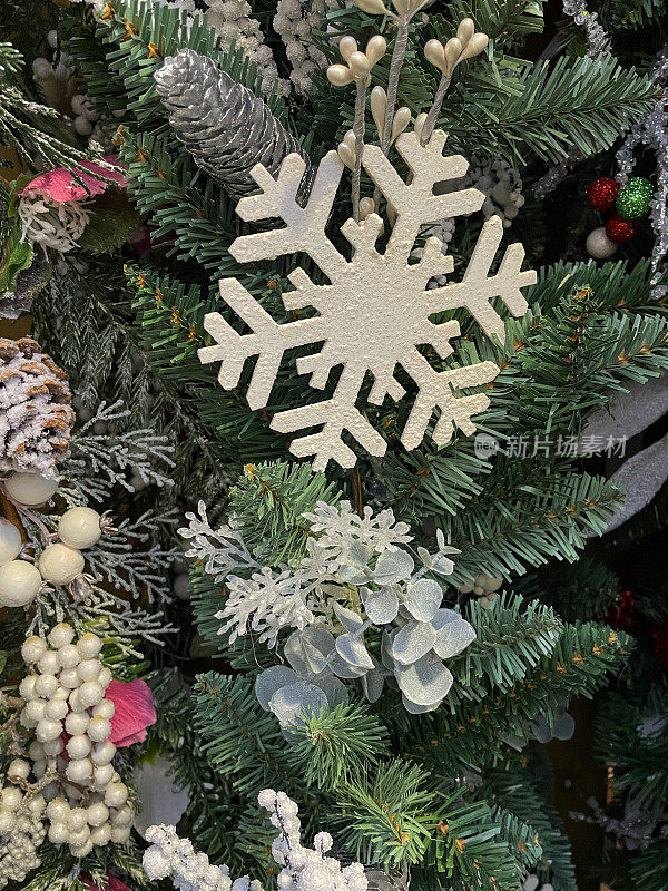 图像白色的雪花装饰物挂在人工圣诞树上，绿色塑料云杉针，白色的浆果串，银色的松果，模糊的白色神仙灯的背景