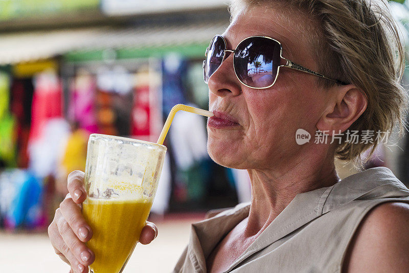 这位50岁的欧洲女游客在海滩上的露天餐厅里用吸管喝芒果鸡尾酒的特写