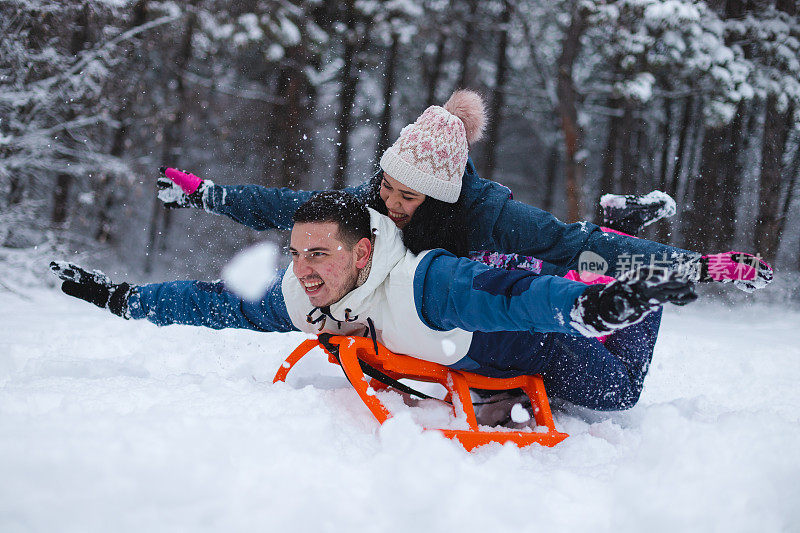 年轻美丽浪漫的夫妇躺在雪橇上在雪地里玩得很开心