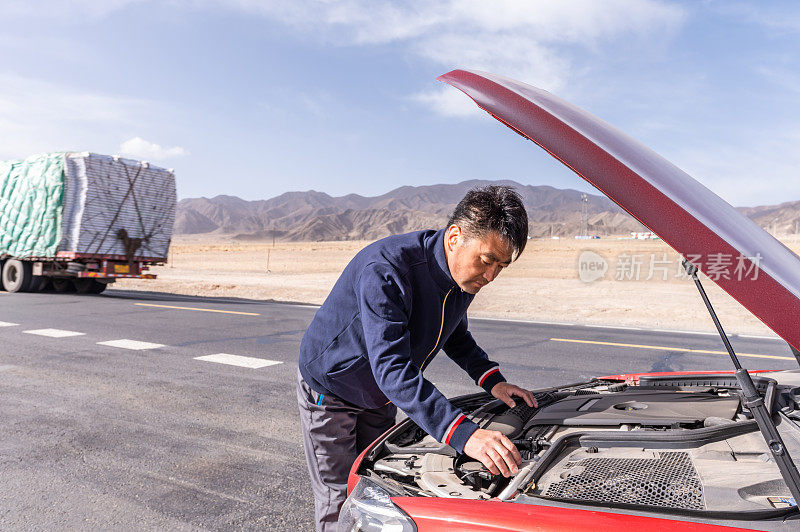 汽车在野外的路上抛锚了，那个亚洲中年男子正在修理汽车