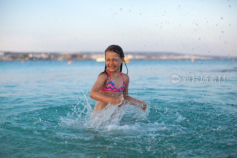 一个年轻快乐的女孩在蓝色的大海游泳，微笑，在水滴中玩，跳跃，在一个炎热的夏天度假，在清澈的水的飞溅中玩得很开心，文字空间