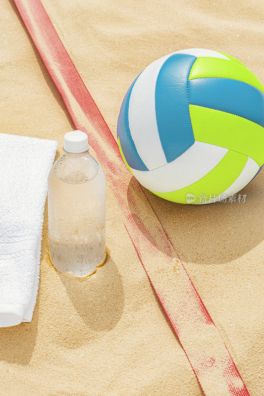 沙滩排球旁边放着一条毛巾，沙滩上放着一瓶水