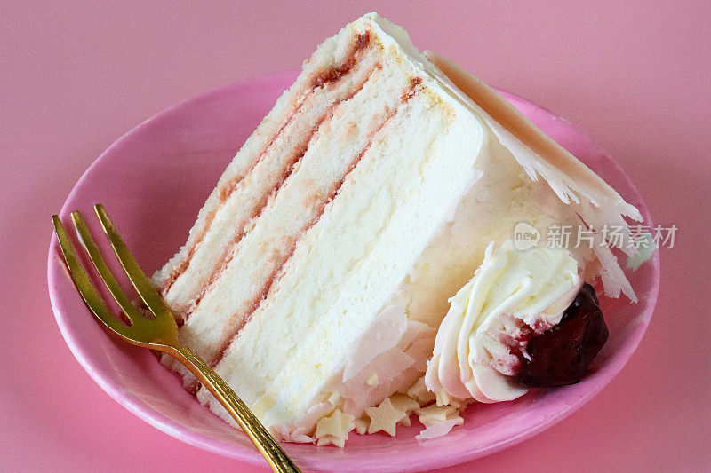天使食物蛋糕切片的特写图像，四个蛋糕层由果酱和鲜奶油在粉红色的盘子上用叉子分开，管道奶油花环，白巧克力星星和樱桃果酱，粉红色的背景，重点在前景