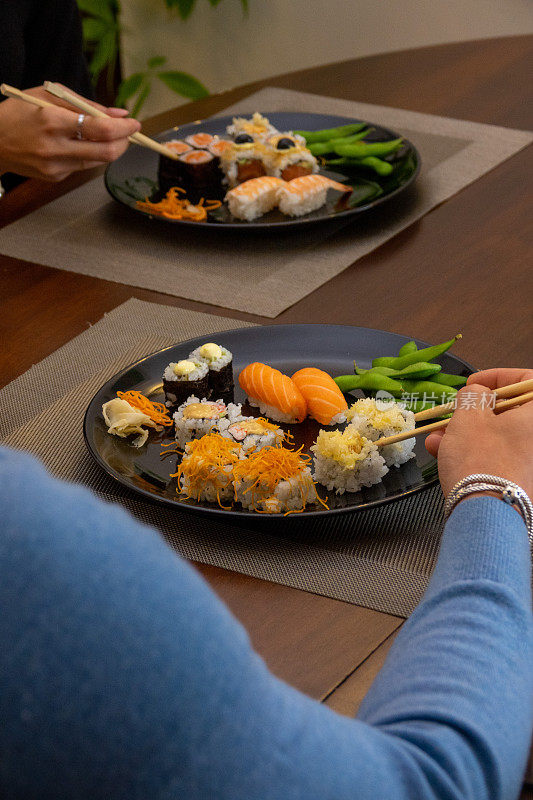 一对夫妇在餐桌上用筷子吃寿司