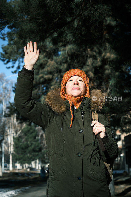 在阳光明媚的冬日小镇街道上，一名女子正在向某人打招呼