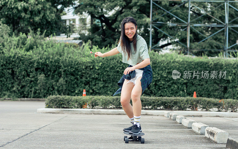 肖像美丽的运动亚洲女滑冰运动员穿着潮衬衫与短裤，微笑与幸福，站在滑板和户外玩与复制空间。活动和冒险概念。