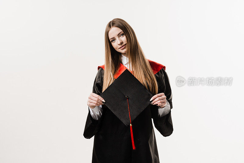 身着黑色毕业服的硕士女研究生手持白底帽。年轻迷人的女子大学毕业。