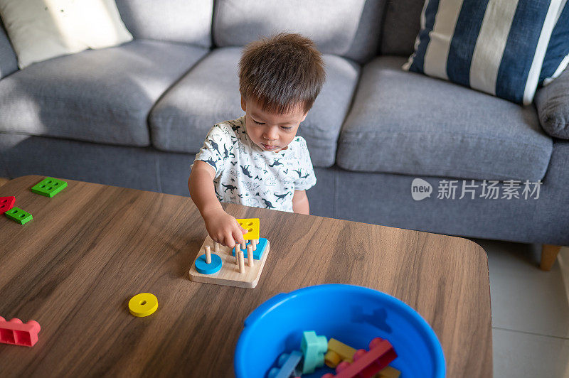 小男孩站在家里的桌子旁，玩着彩色的分类和形状堆叠玩具