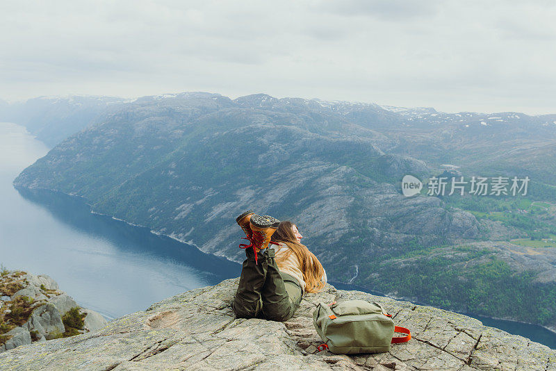 背着背包的女人在悬崖边放松，欣赏挪威吕瑟峡湾田园诗般的景色