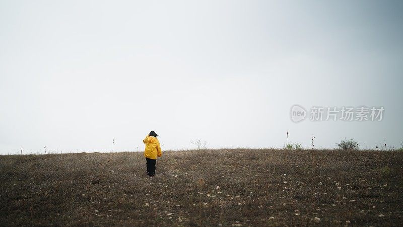 一名女子穿着黄色雨衣，在寒冷多雨的天气里走在大自然和山间