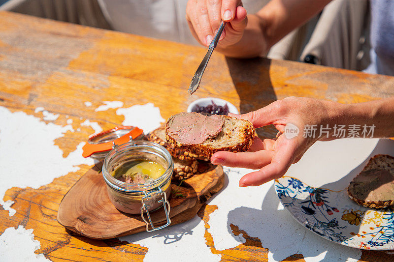 用餐刀将鹅肝酱铺在木桌上的全麦面包片上