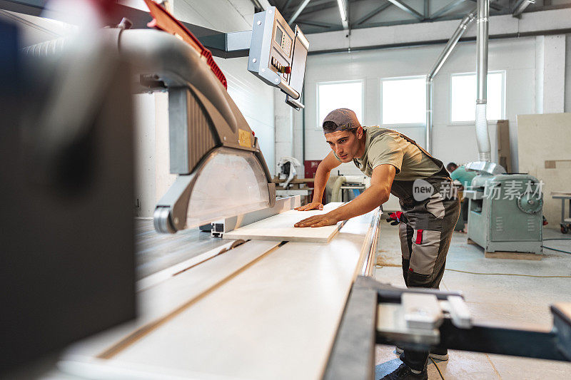 在家具厂，年轻的木匠正在用圆锯切割一块木头
