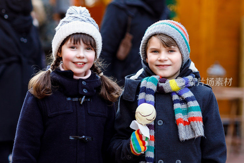 可爱的小女孩和男孩在传统的德国圣诞市场上吃着白巧克力包裹的草莓和苹果串。快乐的孩子，最好的朋友，双胞胎和兄弟姐妹在雪天