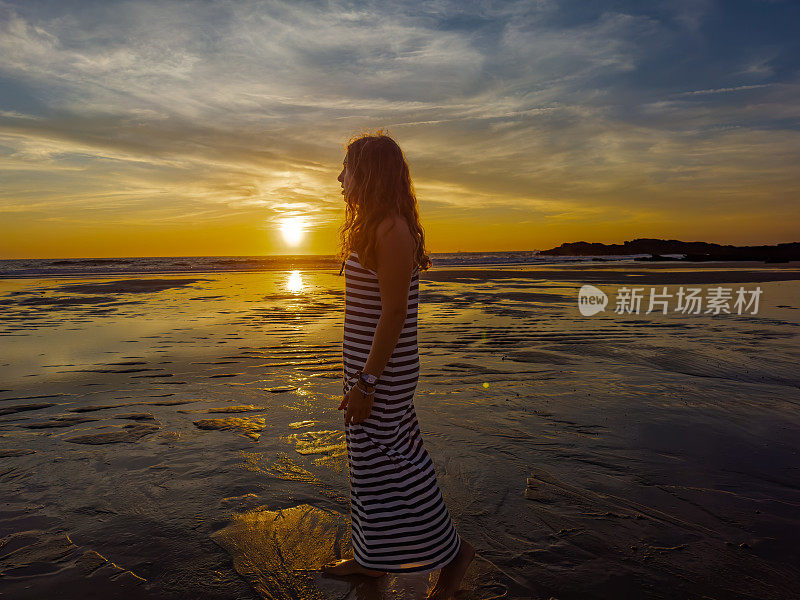 一个年轻美丽的女孩在日落时分漫步在葡萄牙的海滩上