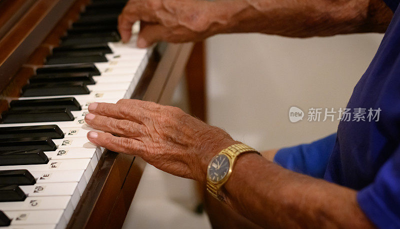 年长的成年男子双手若有所思地弹奏着一架立式钢琴