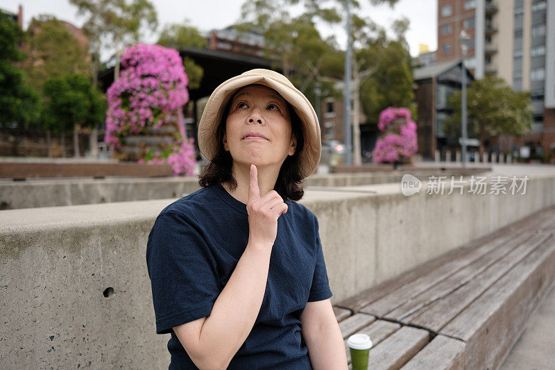 一个亚洲女人在户外微笑着抬头思考