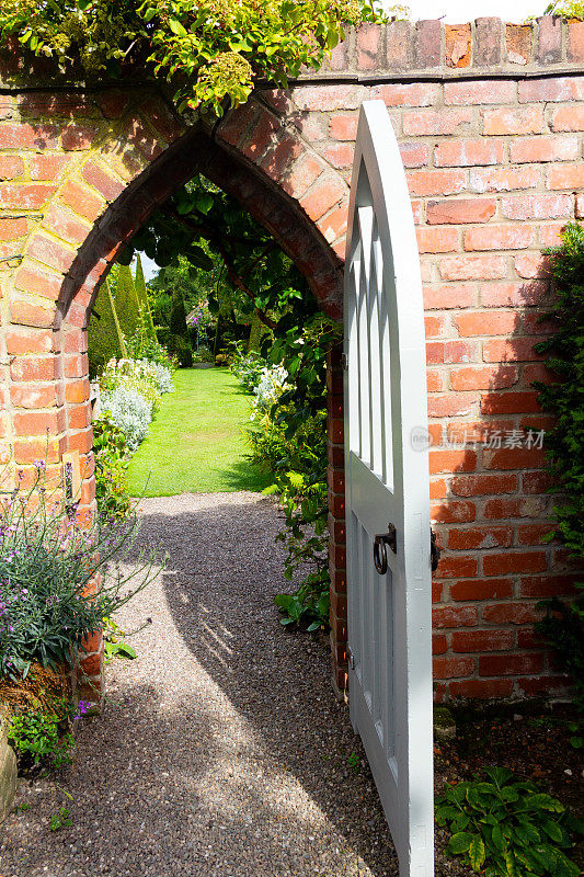通往天堂的大门，古老的砖墙上的拱形白色木门通向美丽的草坪花园。