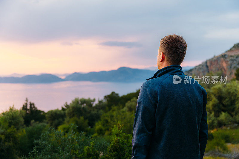 男子欣赏神奇的日落俯瞰大海和山脉