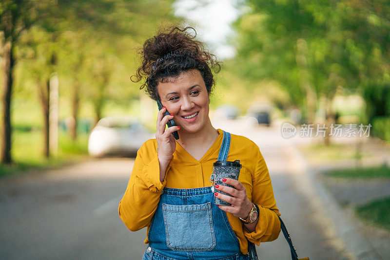 一个轻松的卷发女人一边走一边打电话。