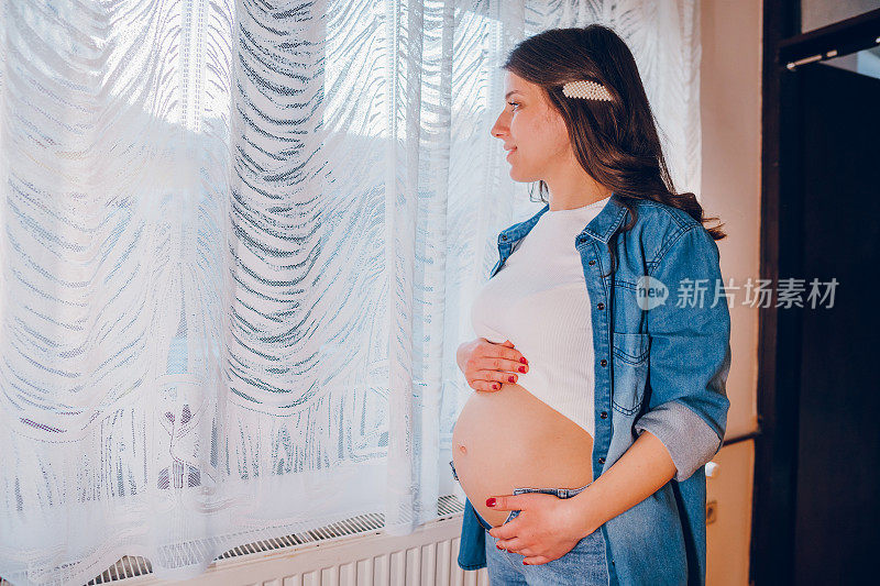 一位孕妇站在窗边，抱着自己的肚子