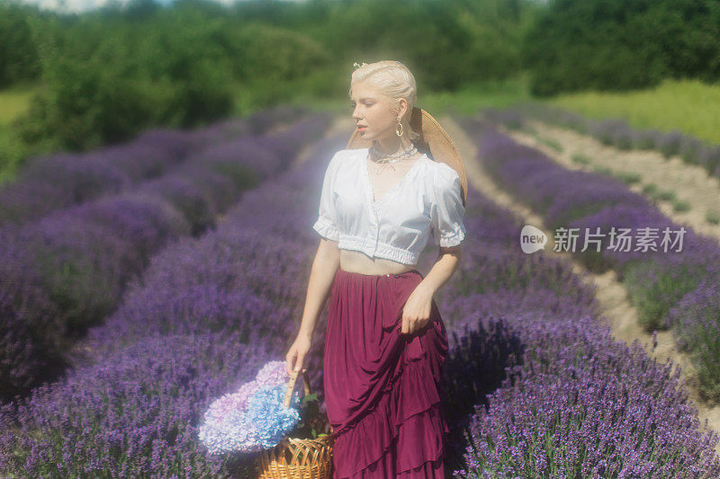 穿紫色裙子的金发女人站在薰衣草地里。夏花