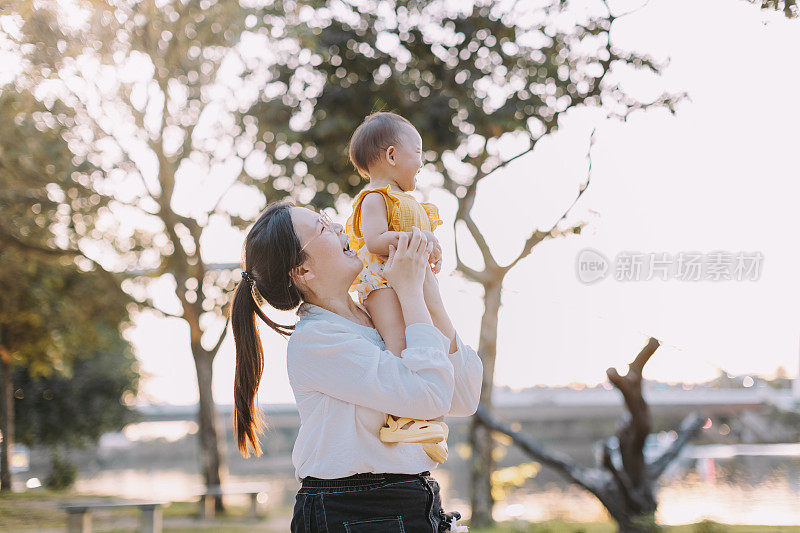 一位亚洲母亲把女儿抱在肩上，给她挠痒痒。库存图片