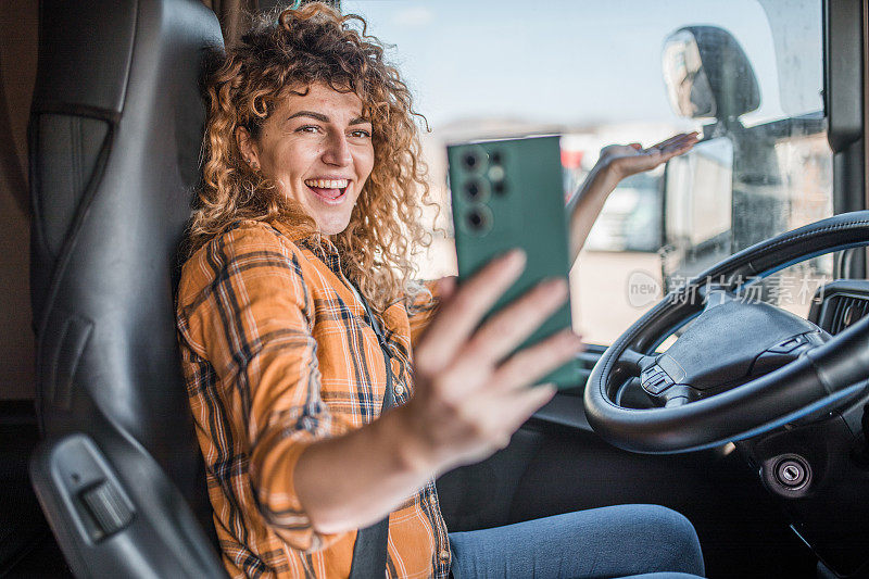 一位微笑着的女卡车司机用手机打视频电话，向她的朋友们展示她现在的位置