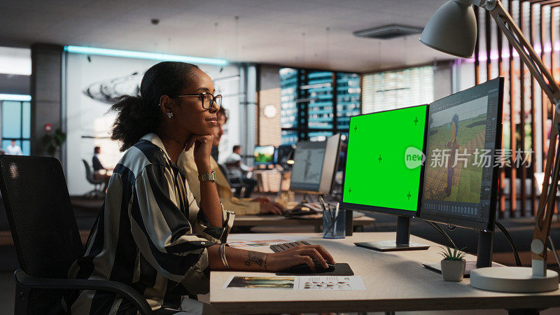 女性黑人游戏设计师使用桌面电脑绿屏Chromakey显示，设计角色在3D建模软件的生存视频游戏。在游戏开发办公室工作的女性