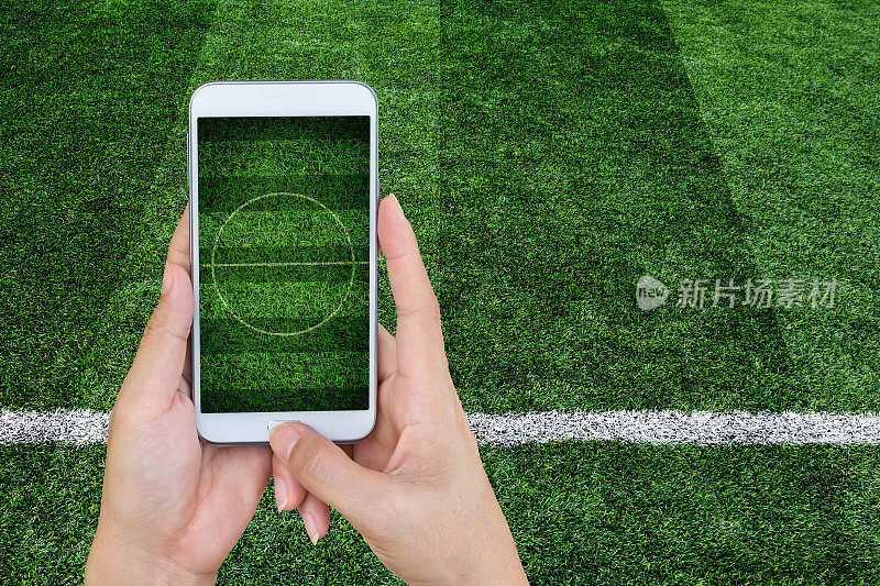 手持智能手机与足球体育场屏幕。