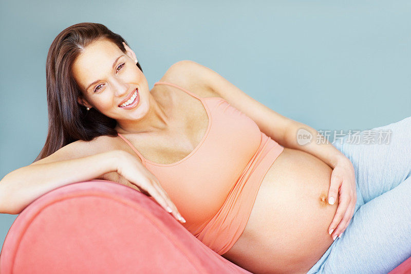 迷人和快乐的年轻孕妇放松在沙发上