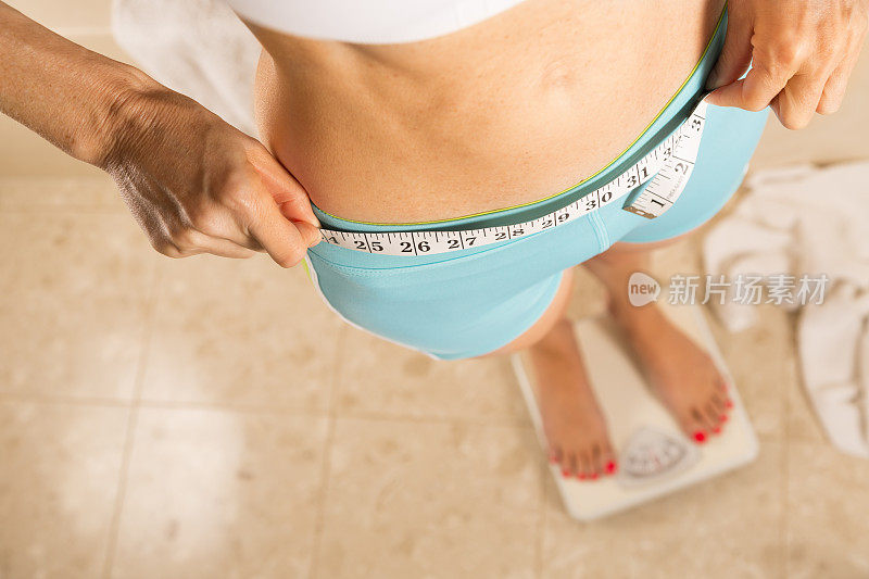 健康生活方式:注重体重的女性用卷尺测量腰围。