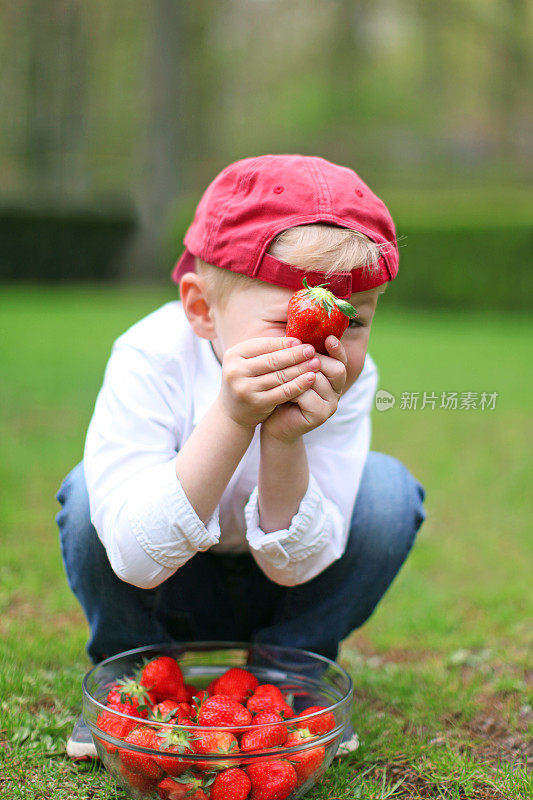 顽皮的男孩把脸藏在草莓后面