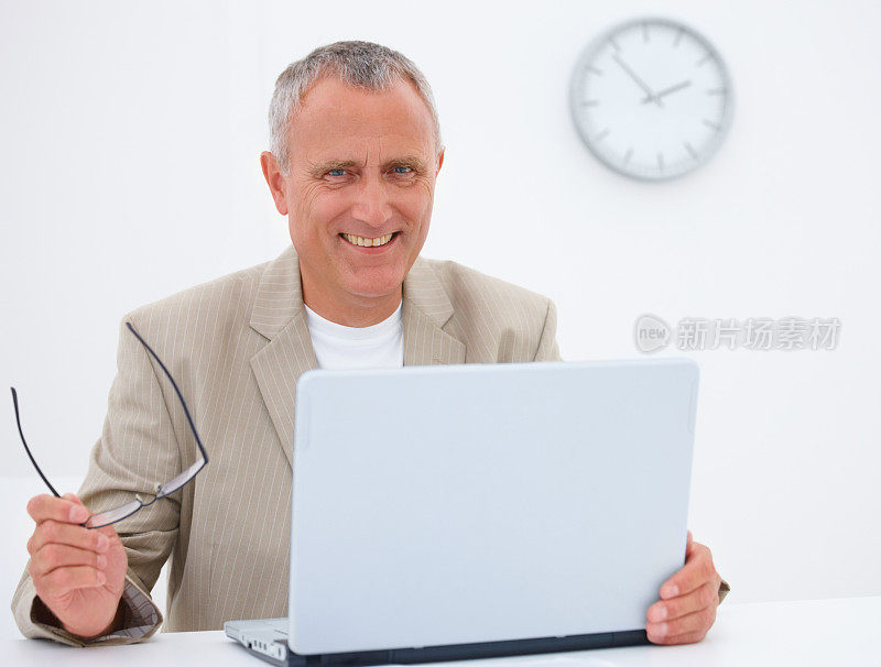 微笑的高级商务人士使用笔记本电脑和拿着眼镜