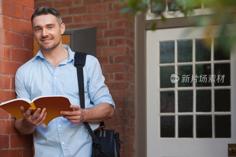 年轻的男学生拿着一本书在大学走廊里